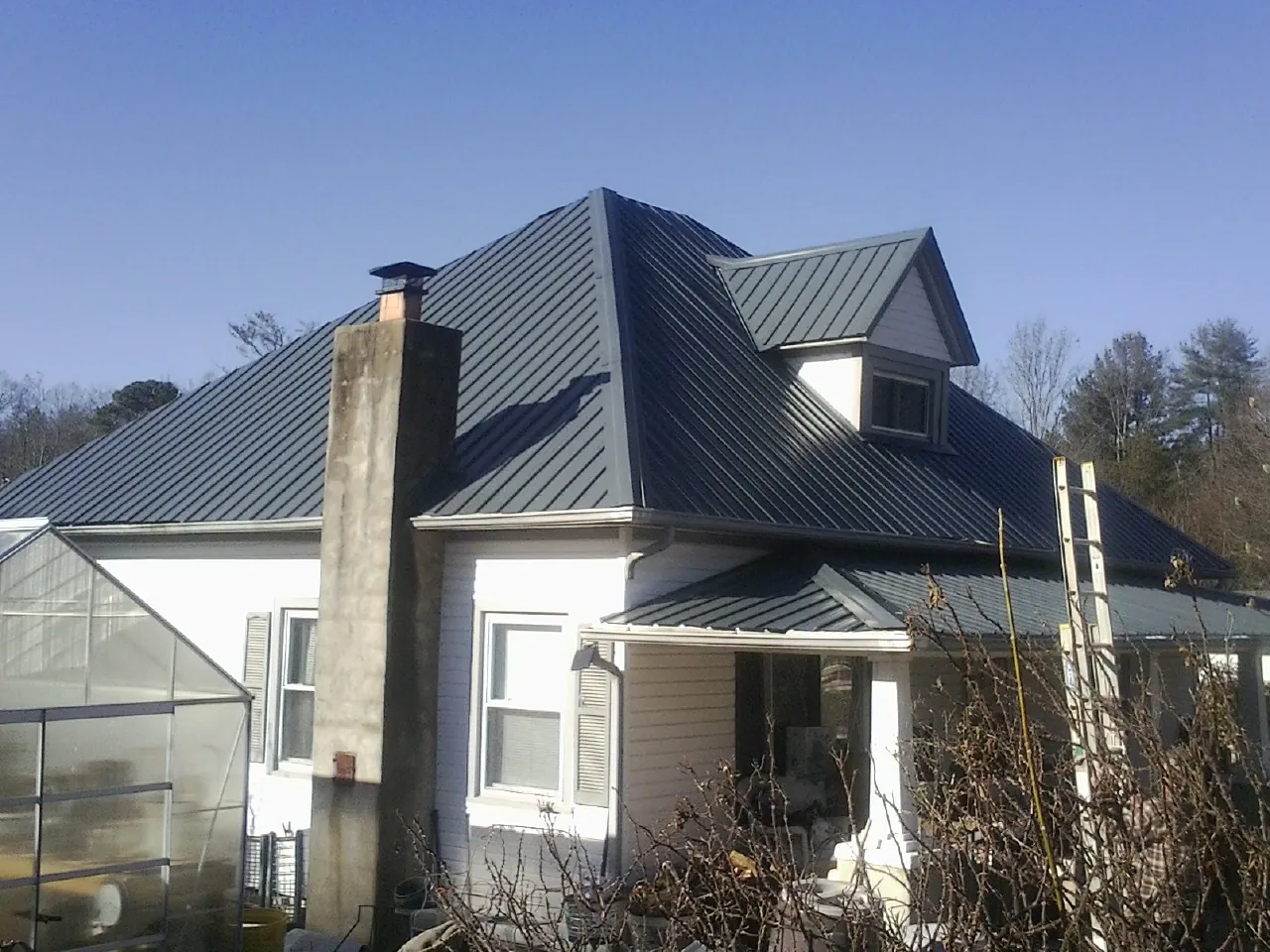 Dark blue standing seam metal roof on a white farmhouse with dormer — Slate & Tile Roof Repair by Roofing Brothers in Meldrim