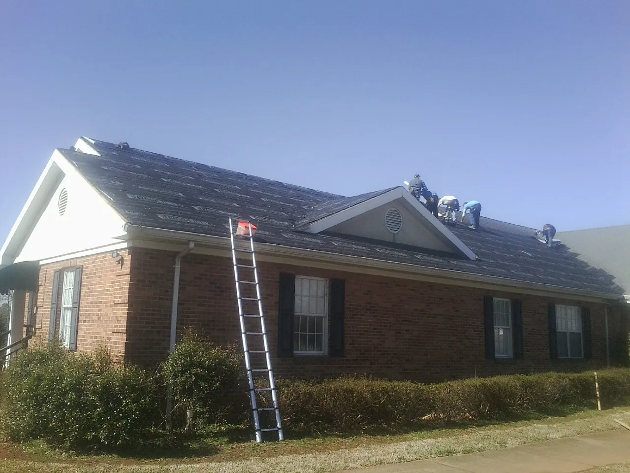 Crew tearing shingles off a brick ranch roof with a ladder set — Emergency Roof Repair work by our crew in Meldrim