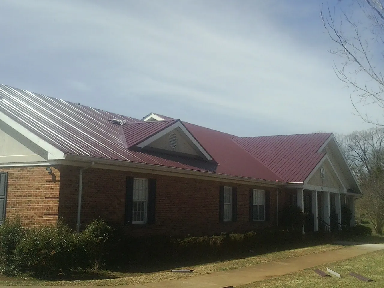 Red metal roof with gabled entries on a long brick building, from a Hail Damage Roof Repair job in Meldrim
