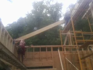 Carpenter raising a rafter beam on a new second story frame in Meldrim