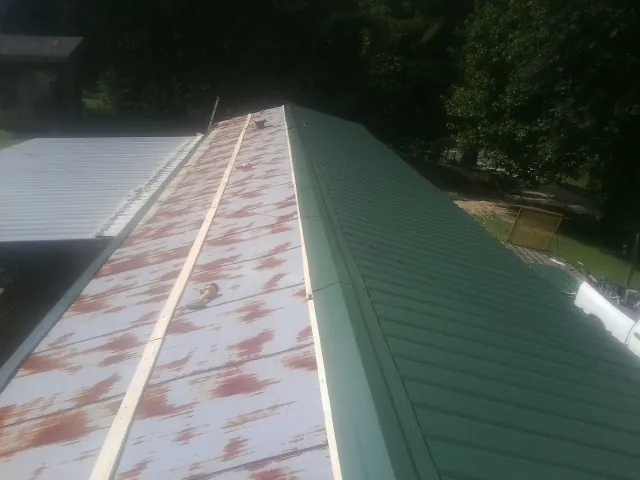 Old rusted panels beside newly installed green metal roofing — Wind Damage Roof Repair by Roofing Brothers in Meldrim