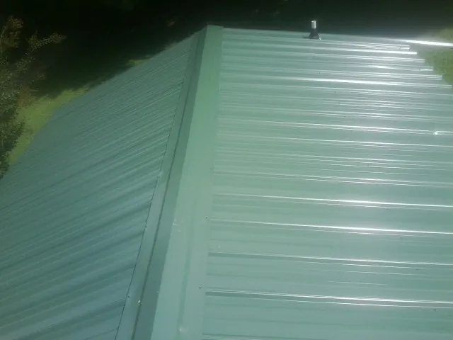 New green metal panels meeting at the ridge of a roof — Flat Roof Repair work by our crew in Meldrim