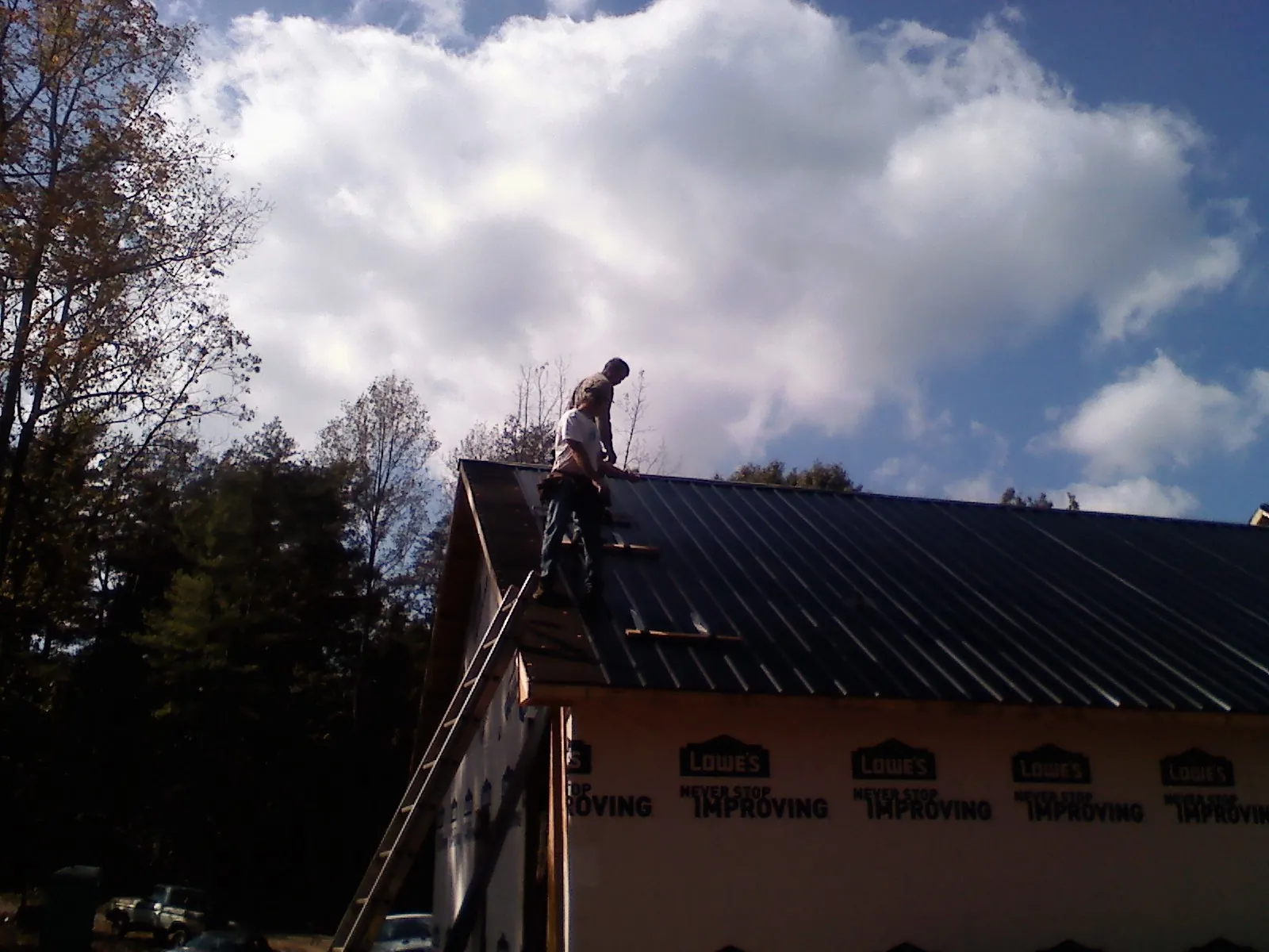 Roofer fastening dark metal panels high against a cloudy sky, from a Roof Inspection job in Meldrim
