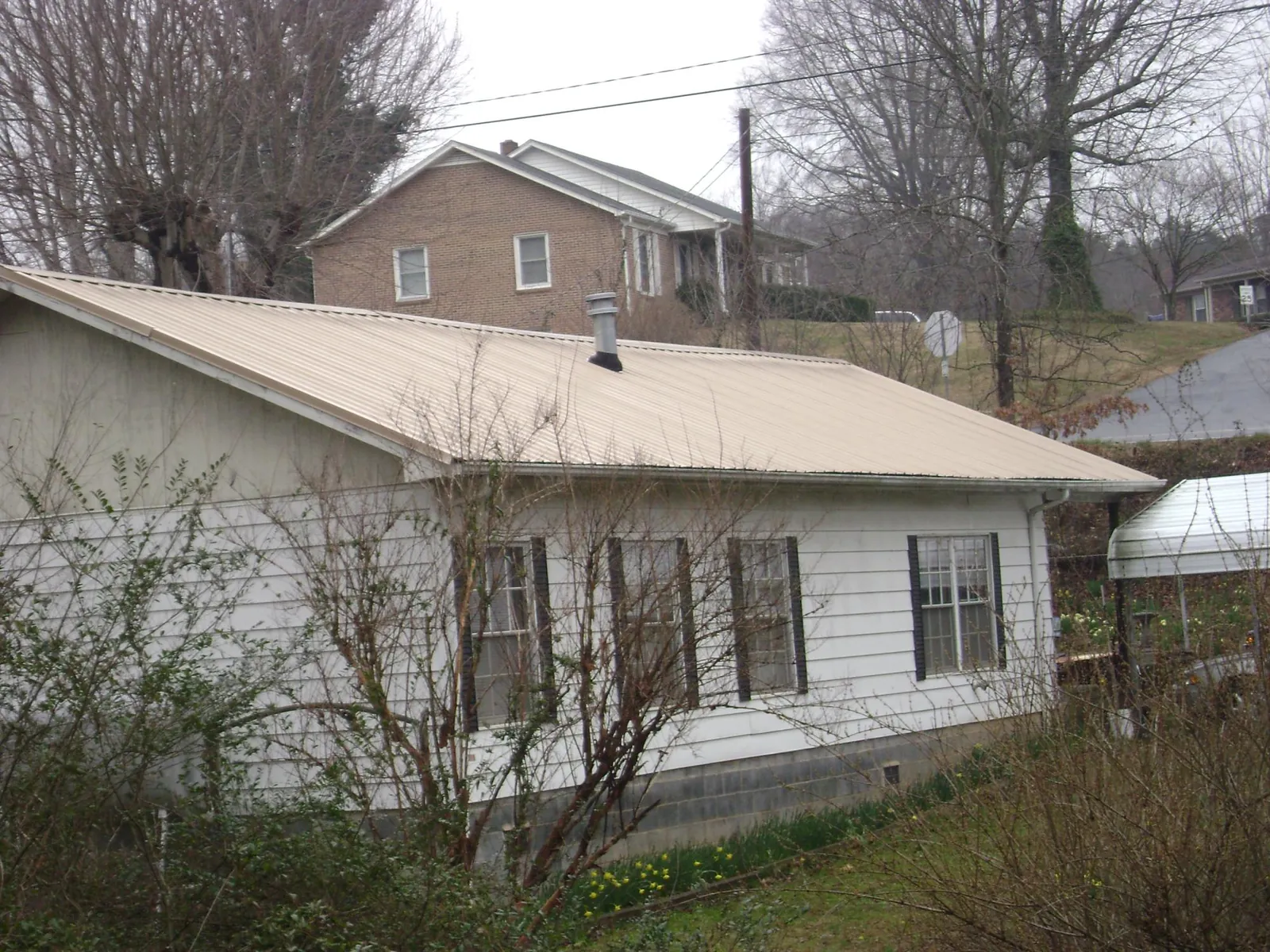 Tan metal roof on a white sided house set into a hillside — Commercial Roofing by Roofing Brothers in Meldrim