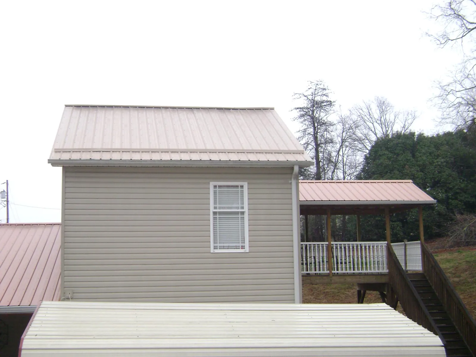 Tan metal roofs on a two story addition and attached porch, from a Roof Replacement job in Meldrim